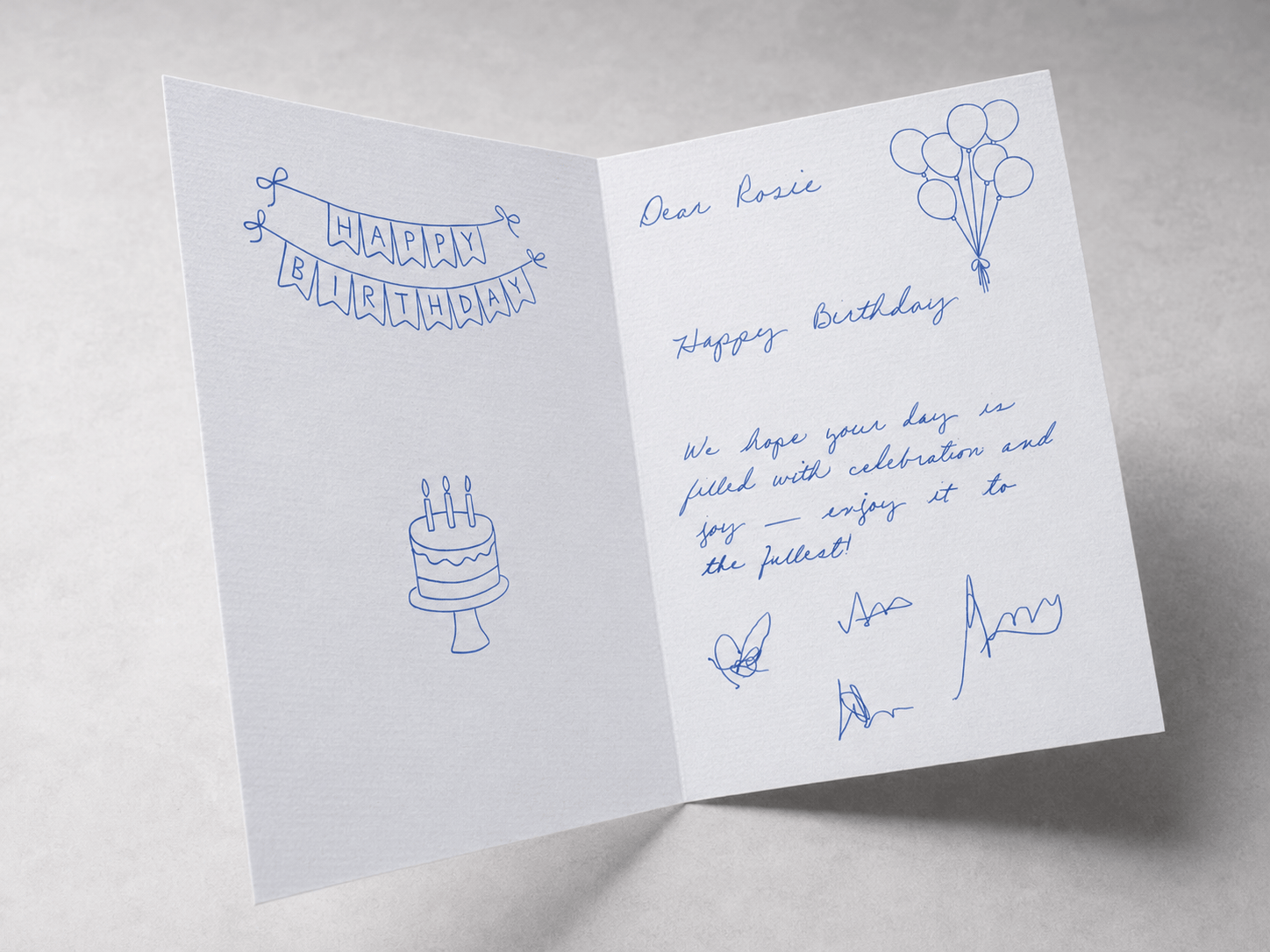 A real handwritten team birthday card with a hand-drawn Happy Birthday banner, balloon doodles, and multiple pen signatures
